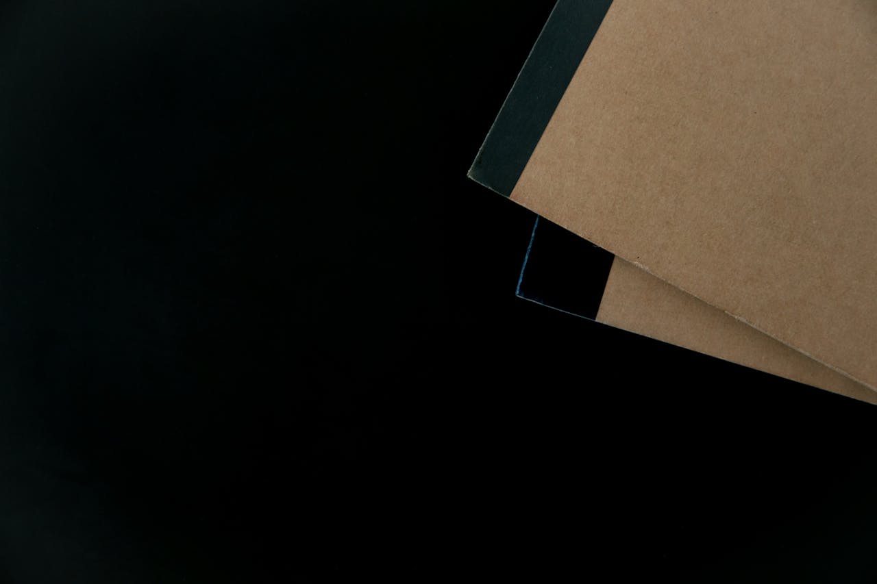 services-01 Brown notebooks with black binding on a dark surface, ideal for stationery themes.